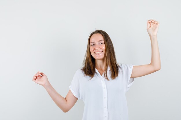 Mujer joven levantando los brazos mientras sonríe en blusa blanca y parece feliz