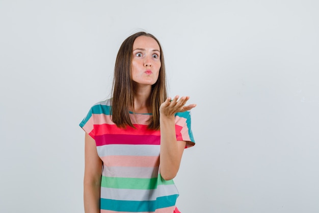 Mujer joven levantando la mano de manera agresiva en camiseta y mirando enojado, vista frontal.