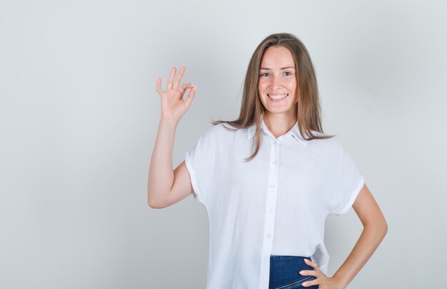 Mujer joven levantando la mano y sonriendo en camiseta blanca