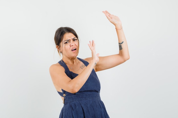 Mujer joven levantando las manos de manera preventiva en vestido y mirando preocupado