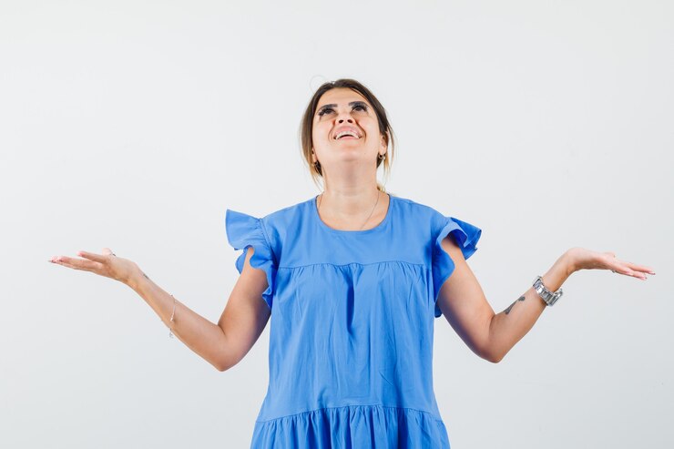 Foto gratuito mujer joven levantando las manos mientras mira hacia arriba con vestido azul y mirando agradecido