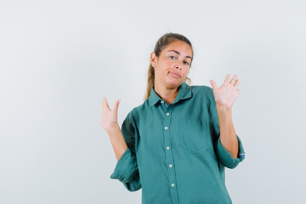 Mujer joven levantando las manos en pose de rendición en blusa verde y luciendo lindo