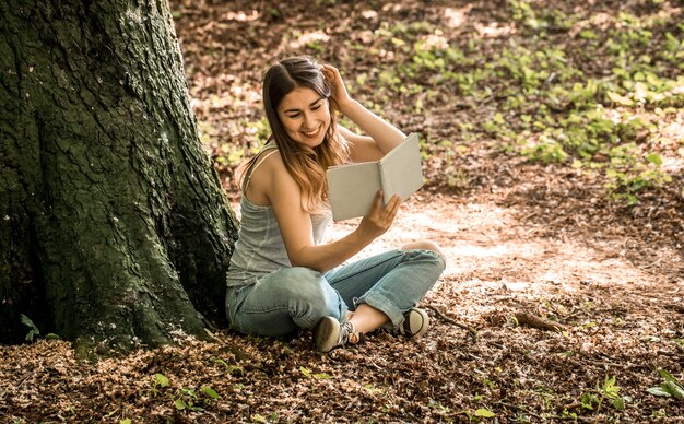 Mujer joven leyendo un libro cerca de un árbol