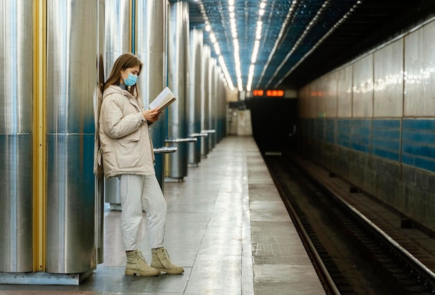 Mujer joven leyendo un libro en una estación de metro