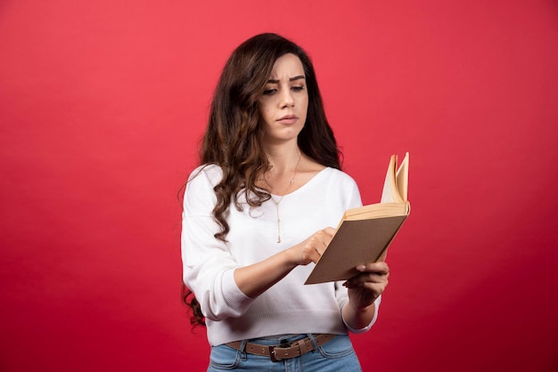 Mujer joven leyendo un libro interesante sobre un fondo rojo. Foto de alta calidad