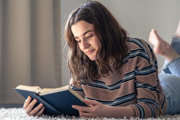 Una mujer joven leyendo un libro mientras está acostada en el suelo en casa