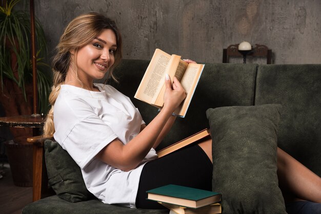 Mujer joven leyendo un libro y mirando al frente en el sofá.