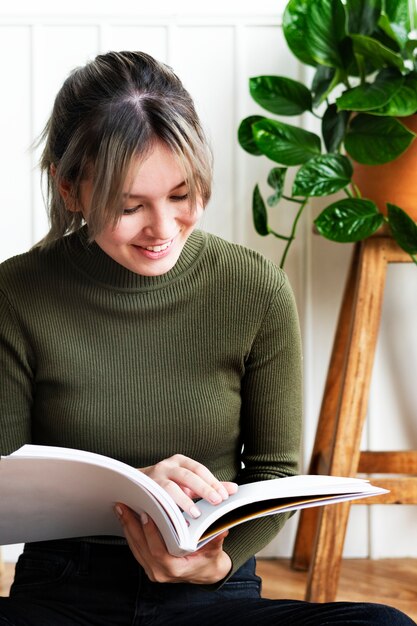 Mujer joven leyendo un libro sobre jardinería rodeado de plantas en macetas