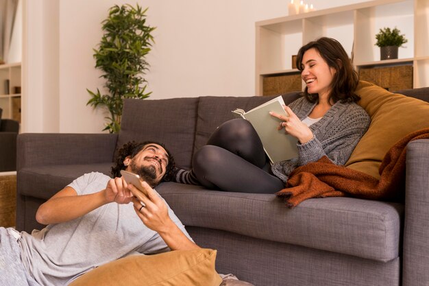 Mujer joven leyendo en la sala de estar junto a su marido