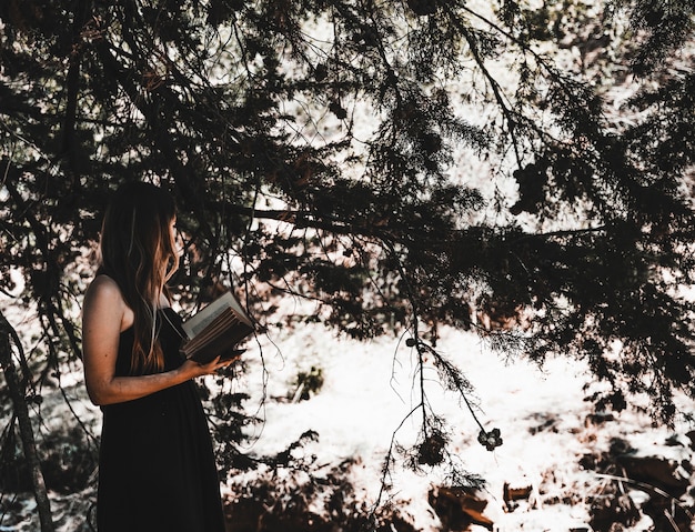 Foto gratuita mujer joven con libro de pie en el bosque