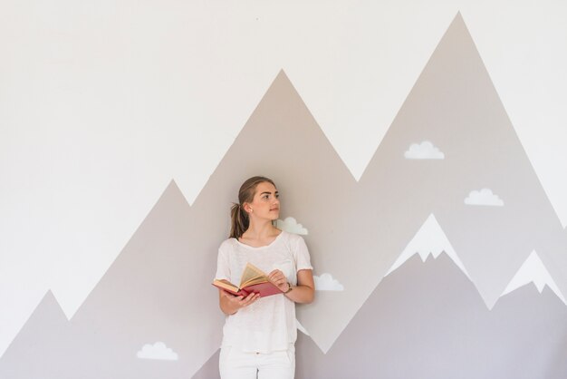 Mujer joven con libro de pie contra la pared de graffiti