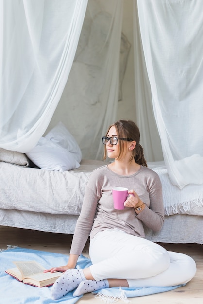 Mujer joven con libro sosteniendo la taza de café mirando a otro lado