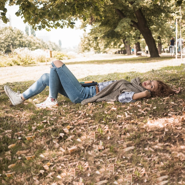 Mujer joven con libros mentir parque hierba