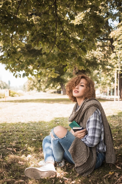 Mujer joven con libros sentado en el suelo del parque