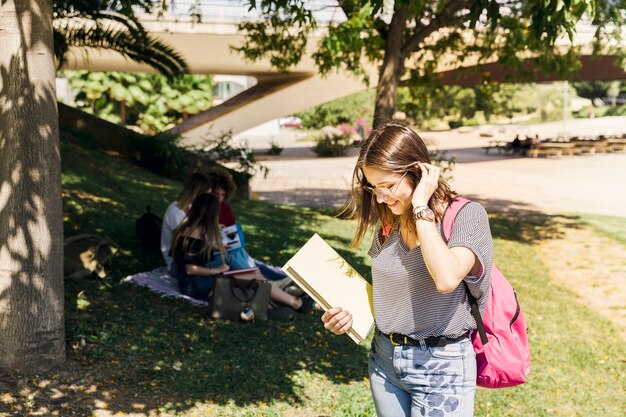 Foto gratuita mujer joven con libros de texto y mochila en el parque