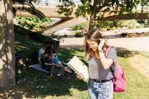 Foto gratuita mujer joven con libros de texto y mochila en el parque