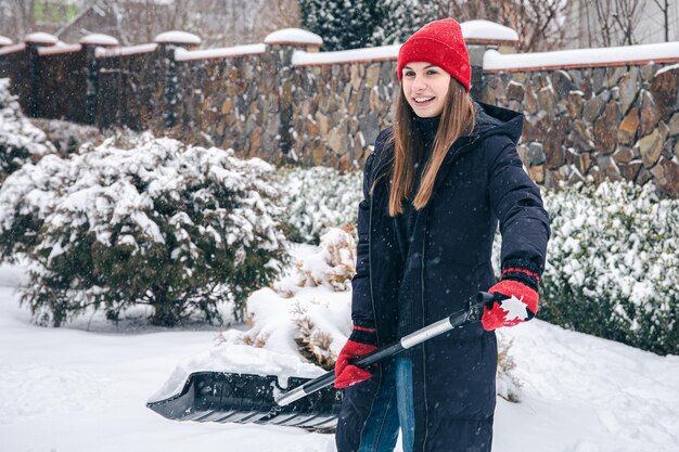 Mujer joven limpia la nieve en el patio en tiempo de nieve