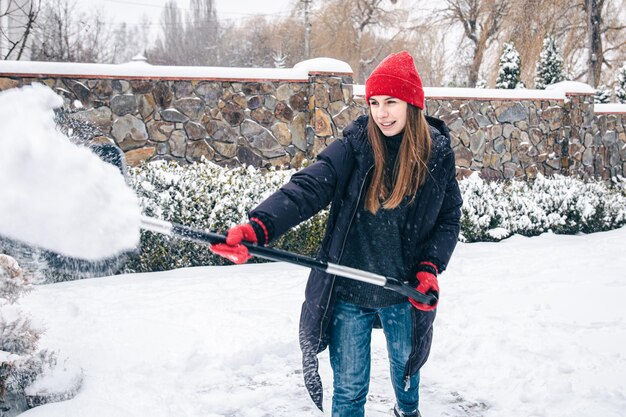 Mujer joven limpia la nieve en el patio en tiempo de nieve