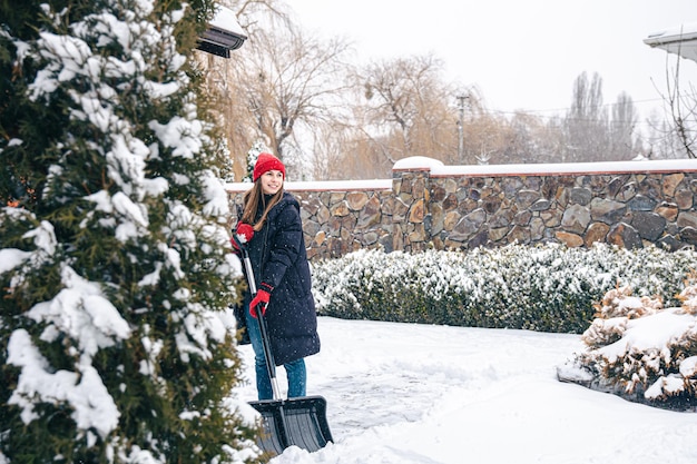 Mujer joven limpia la nieve en el patio en tiempo de nieve