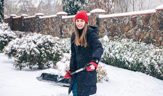 Mujer joven limpia la nieve en el patio en tiempo de nieve