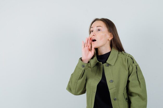 Mujer joven llamando a alguien con chaqueta verde y mirando concentrado. vista frontal. espacio para texto