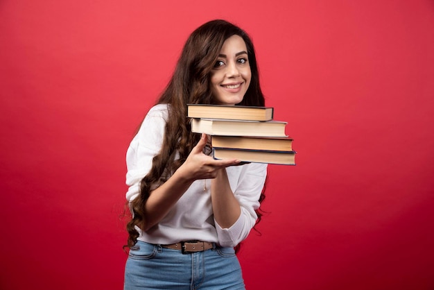 Mujer joven llevando libros sobre un fondo rojo. Foto de alta calidad