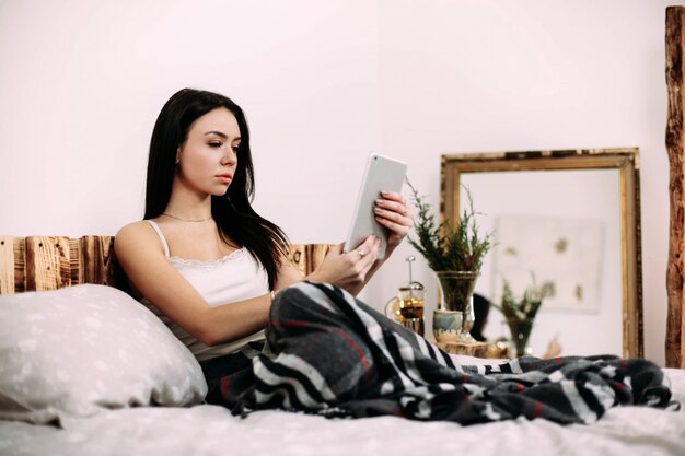 La mujer joven magnífica lee algo en su iPad que miente debajo de la tela escocesa