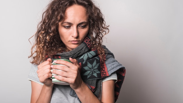 Mujer joven mal con la bufanda alrededor de su cuello que sostiene la taza de café