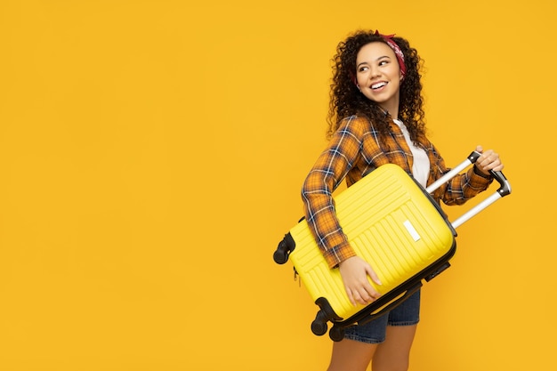 Mujer joven con maleta sobre fondo amarillo