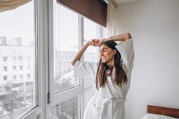 Mujer joven en la mañana que se extiende por la ventana