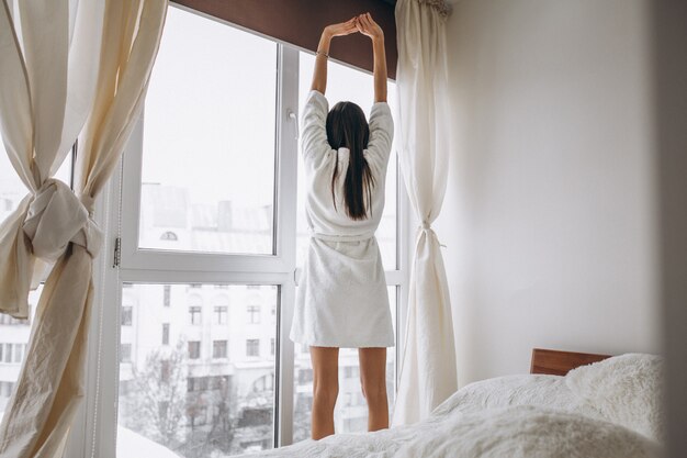 Mujer joven en la mañana que se extiende por la ventana