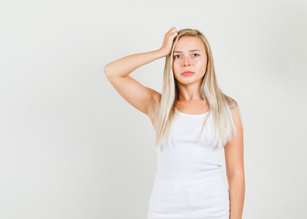 Mujer joven con la mano en el cabello en camiseta blanca y mirando molesto.