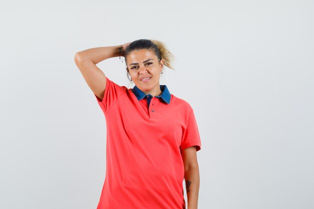 Mujer joven con la mano en la cabeza en camiseta roja y mirando exhausto, vista frontal.