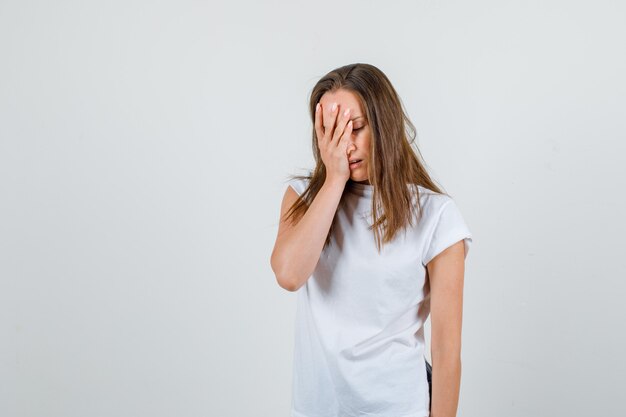 Mujer joven con la mano en la cara en camiseta blanca, pantalones cortos y aspecto cansado