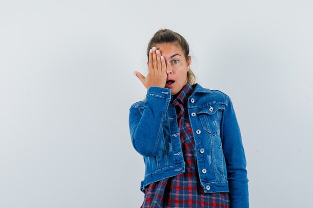 Mujer joven con la mano en el ojo en camisa, chaqueta y mirando asombrado. vista frontal.