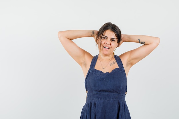 Foto gratuita mujer joven, manos de valor en cartera, detrás de la cabeza, en, vestido, y, mirar, relajado