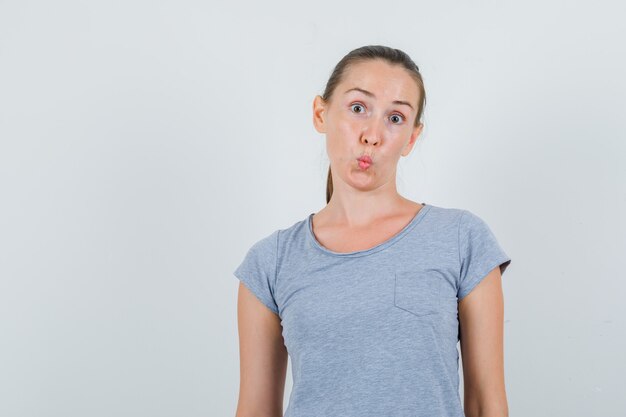 Mujer joven manteniendo los labios doblados en camiseta gris y mirando confundido, vista frontal.