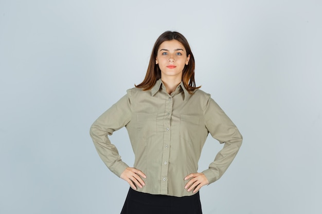 Foto gratuita mujer joven manteniendo las manos en la cintura en camisa, falda y mirando confiado