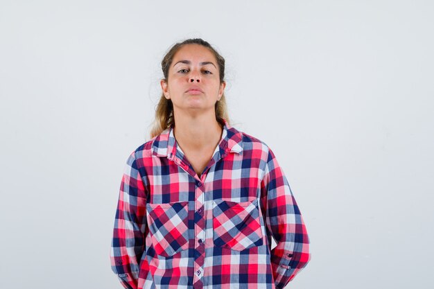 Mujer joven manteniendo las manos detrás de la espalda en camisa casual y mirando triste. vista frontal.