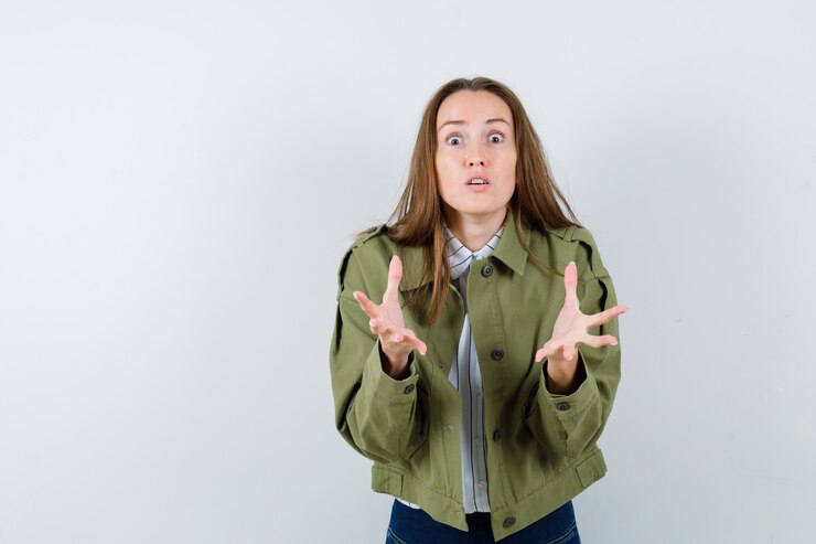 Foto gratuito mujer joven manteniendo las manos en gesto de perplejidad en camisa, vista frontal.