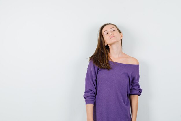 Mujer joven manteniendo los ojos cerrados con camisa violeta y buscando pacífica. vista frontal.