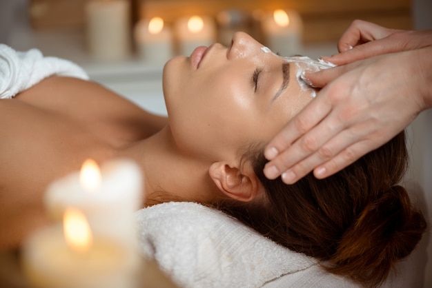 Mujer joven en la máscara para la cara relajante en el salón de spa.