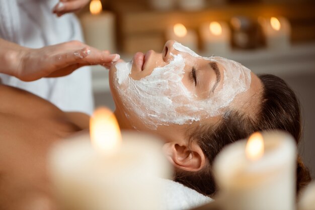 Mujer joven en la máscara para la cara relajante en el salón de spa.