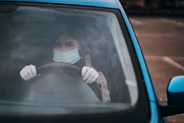 Mujer joven en una máscara y guantes de conducir un coche.