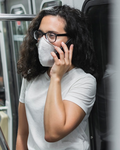 Mujer joven con máscara médica hablando por teléfono en el metro