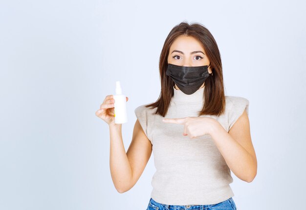 Mujer joven con una máscara médica negra apuntando a un spray.