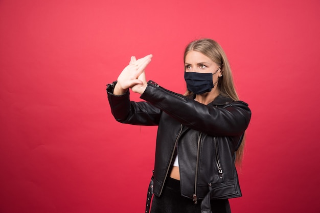 Mujer joven en máscara médica de pie y cruzando las manos haciendo señal negativa de rechazo