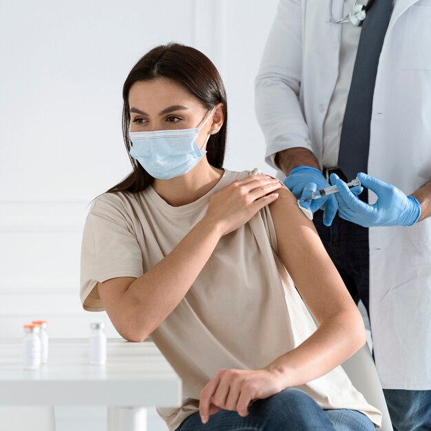 Mujer joven con máscara médica siendo vacunada por médico