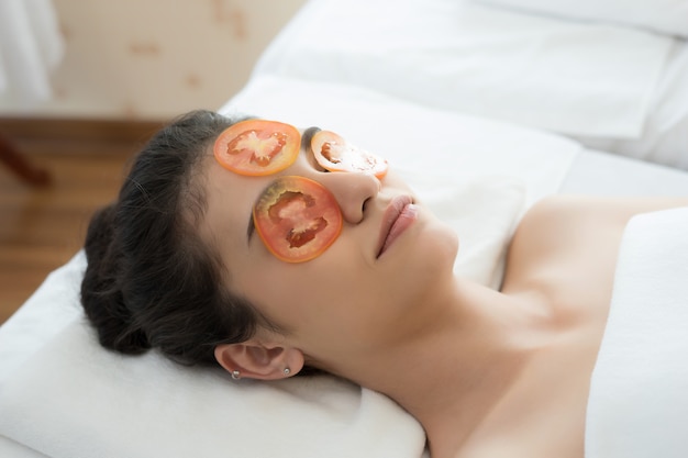 Mujer joven con máscara de tomates frescos en el spa.