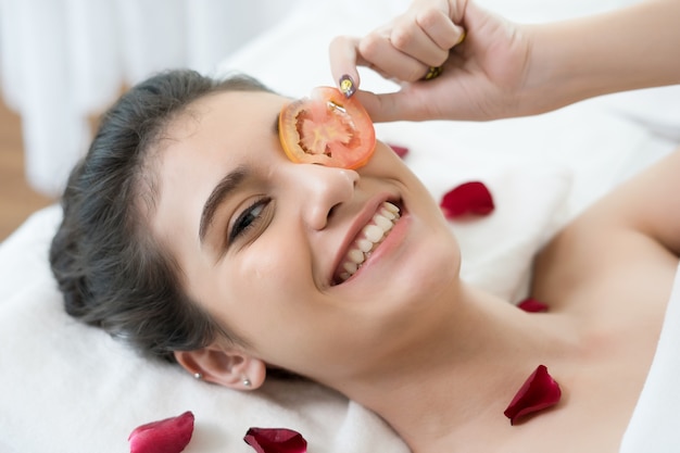 Mujer joven con máscara de tomates frescos en el spa.